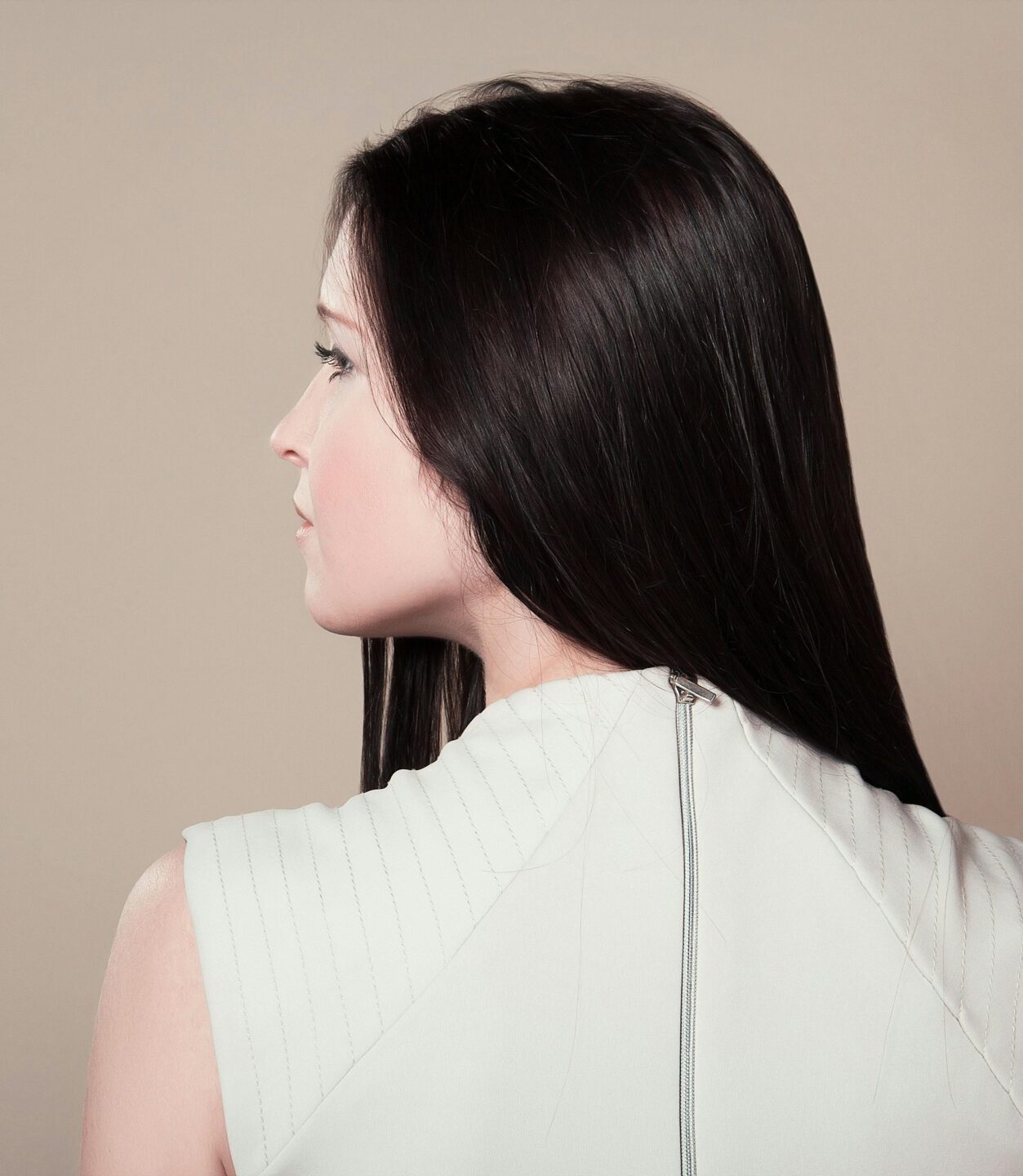 Profile view of a brunette woman in white attire indoors on a neutral background.