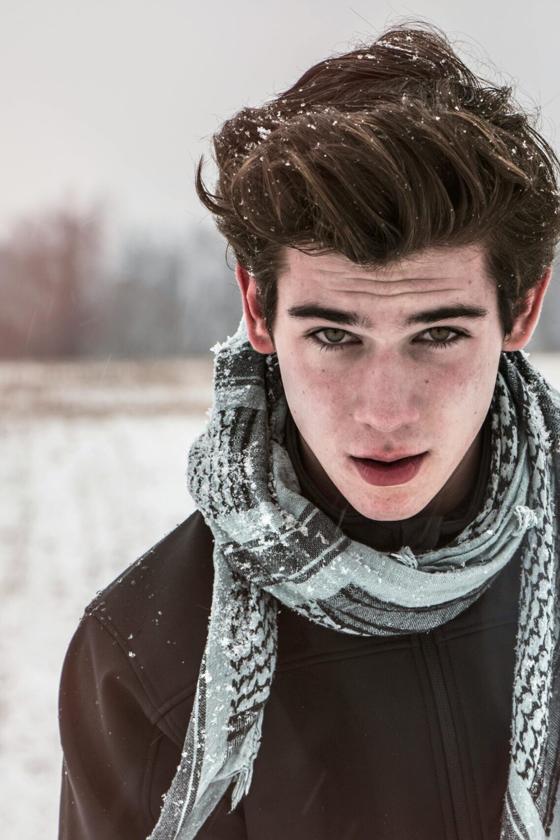 Portrait of a young man outdoors in a snowy field wearing a scarf.
